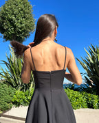 Rochie neagra elegantă scurtă cu bretele și fustă evazată într-un cadru natural.