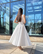 Rochie de mireasa midi albă cu buzunare și centură delicată, design modern și elegant.