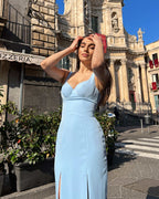 Rochie eleganta albastra cu decolteu și slit dublu în fața unei clădiri istorice.