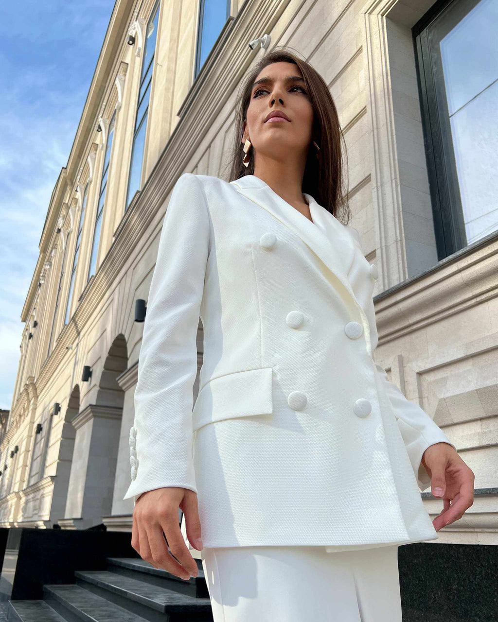 Sacou alb elegant cu două rânduri de nasturi, model cambrat, guler în V, mâneci lungi și buzunare decorative.