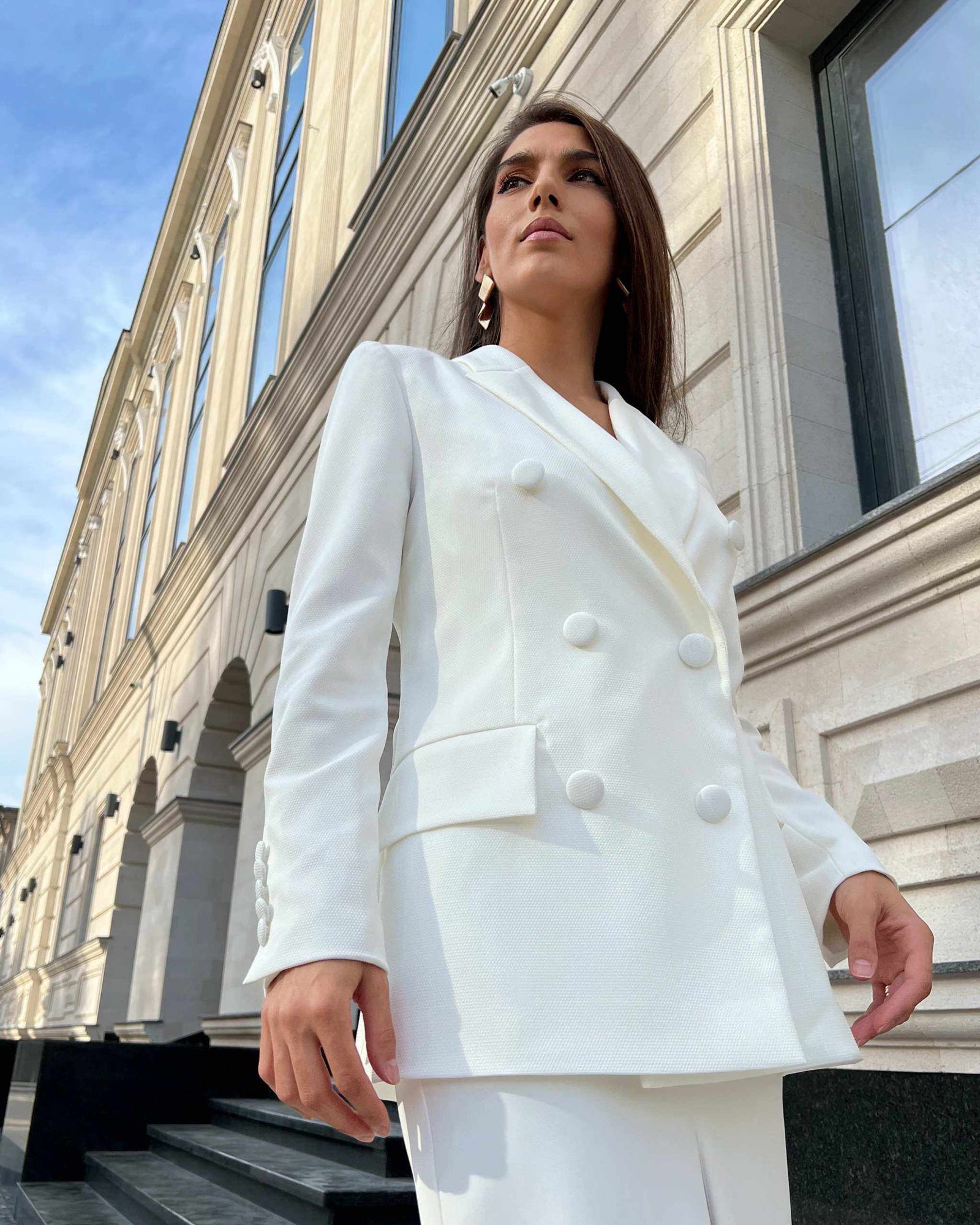 Sacou alb elegant cu două rânduri de nasturi, model cambrat, guler în V, mâneci lungi și buzunare decorative.