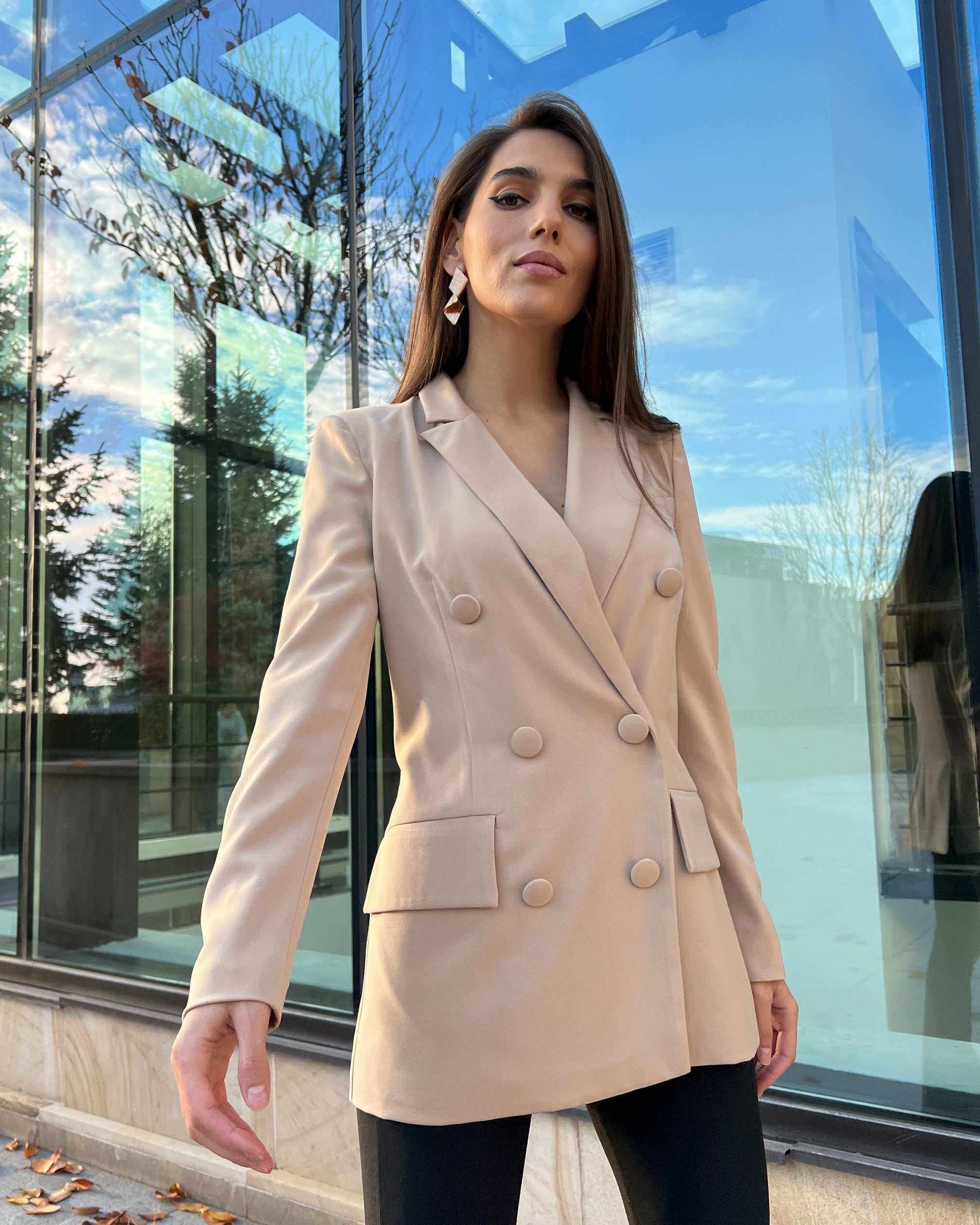 Sacou de costum bej cu două rânduri de nasturi, model cambrat cu guler în V și mâneci lungi.